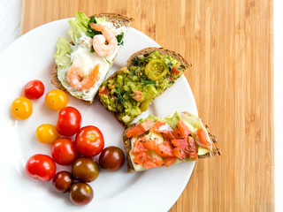 Open sandviches with guacamole, salmon and shrimp and tomato cherry on the plate, wooden background