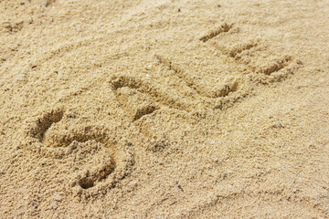 Sale word written on the sand at the beach, natural background
