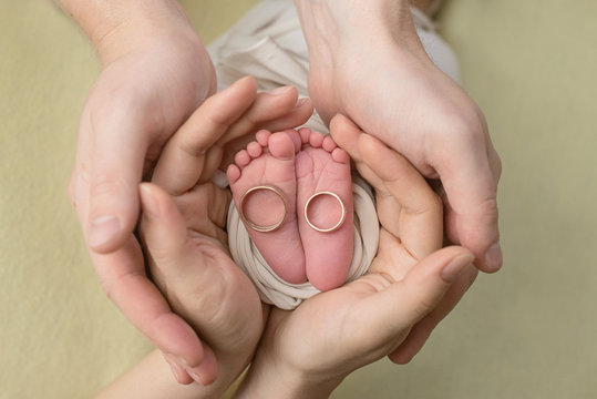 Feet of a newborn baby, toes in the hands of mom and dad,   the first days of life after birth, yellow background, family wedding rings