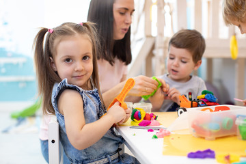 Teacher teaches kids modeling clay in playroom at daycare or kindergarten