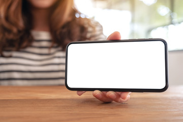 Mockup image of a woman holding and showing white mobile phone with blank screen horizontally on wooden table