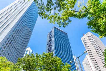 Asia Business concept for real estate, corporate construction and ecology - looking up view of panoramic modern city skyline with blue sky and green tree in shinjuku, tokyo, japan