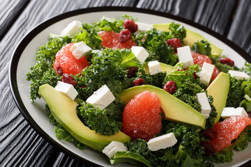 Kale salad with avocado, grapefruit, feta and dried cranberries with lemon dressing close-up on a plate. horizontal