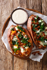 Serving of baked sweet potato filled with fresh kale, bacon and cheese sauce close-up on a plate. Vertical top view