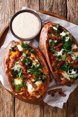Delicious whole baked sweet potato with fresh kale, bacon and cheese sauce close-up on a plate. Vertical top view
