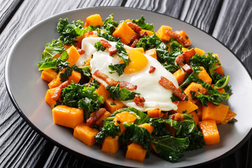 Tasty sweet potatoes with kale cabbage served with bacon and fried egg close-up on a plate. horizontal