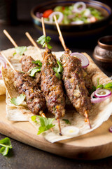 Lula kebab from minced meat (beef, lamb, veal) on pita bread (lavash), shish kebab. With red onion, cilantro and vegetable salad