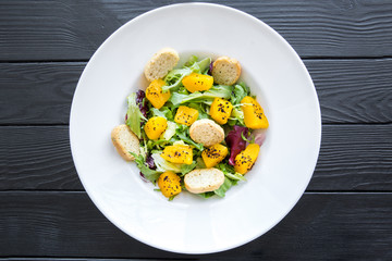 Healthy salad with pumpkin on black table.