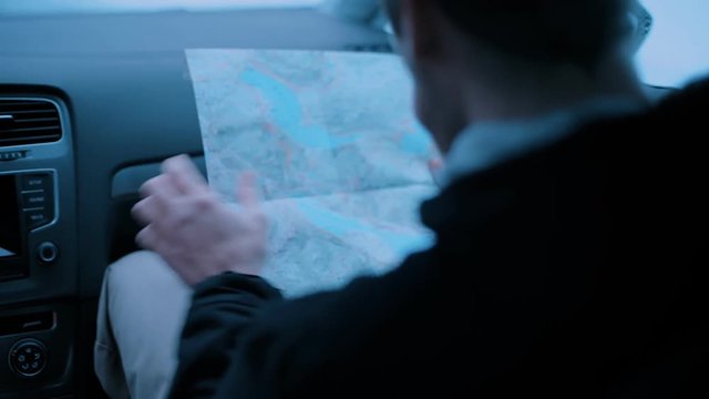Cinematic authentic shot from behind shoulder of young traveller or adventurer navigate through small country winter road, read old vintage paper map look for directions. Wanderlust inspiration