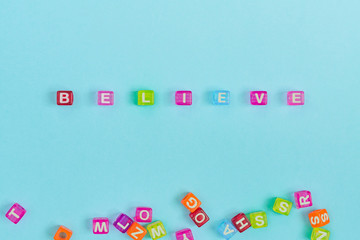believe inscription made of colorful cube beads with letters. Festive blue background concept with copy space..