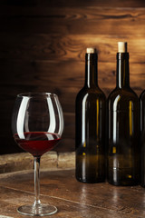 Bottle and glass of red wine on wooden barrel shot with dark wooden background