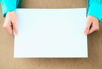 Blank paper in womanэs hands waiting for idea or advertising lettering.