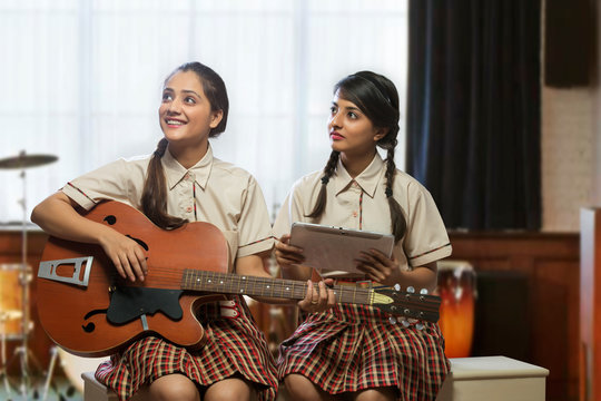 Two happy teenage school girls learning to play guitar in the music room at school	