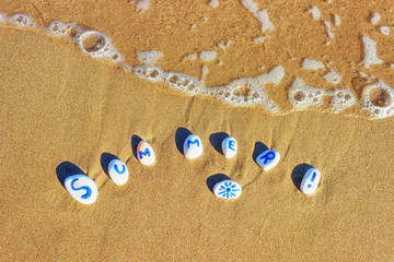 Fototapeta na wymiar Painted sea pebbles on a summer beach in the oncoming wave. Inscription on the stones 