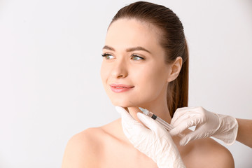 Young woman receiving injection in face on light background