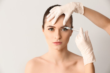 Young woman receiving injection in face on light background