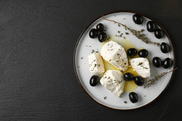 Plate with tasty feta cheese, olive oil and herbs on dark table