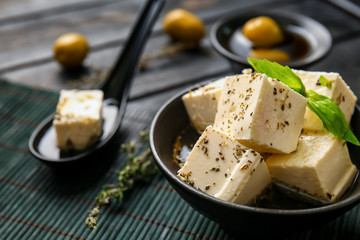 Bowl with tasty feta cheese in olive oil on table