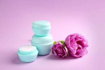Jars of natural cream with tulips on color background