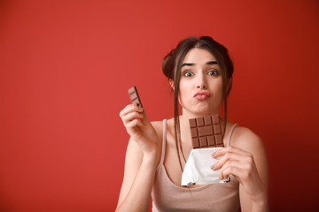 Funny young woman with tasty chocolate on color background