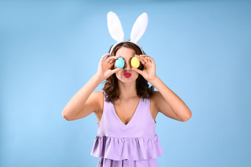 Beautiful young woman with bunny ears and Easter eggs on color background