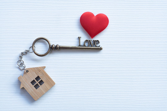House key in heart shape with home keyring on white wood background decorated with mini heart