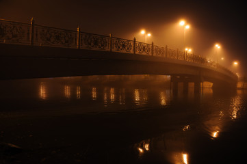 Bridge over the river in the city at night in the fog