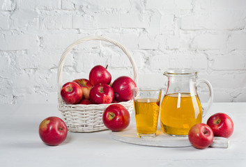 Apple juice in carafe and glass with apples on white table.