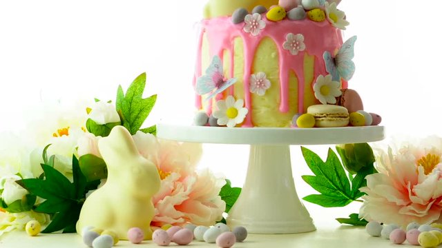 On-trend Easter theme candy land drip cake decorated with lollipops, cand eggs and white chocolate bunny on white background.