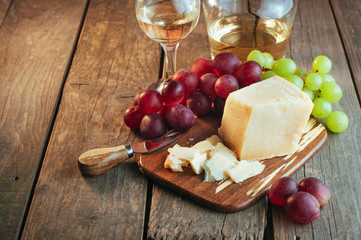 Parmesan cheese on wooden board near white wine and grape with copy space