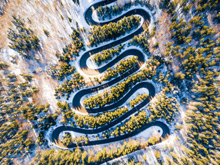 Winding road through the forest, from high mountain pass, in winter time. Aerial view by drone . Romania	