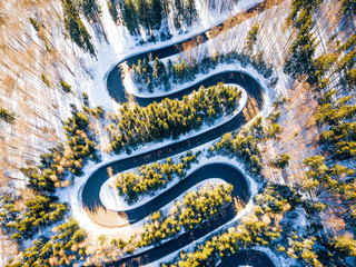 Winding road through the forest, from high mountain pass, in winter time. Aerial view by drone . Romania	