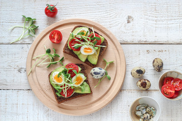 Fototapeta na wymiar Healthy sandwiches with avocado, tomato, quail eggs and sunflowers micro greens (sprouts) on a white wooden background, flatlay