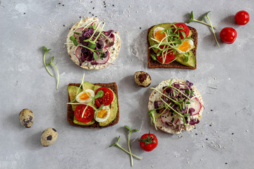 Healthy sandwiches with avocado, tomato, quail eggs, radishes and micro greens (sprouts) on a dark background, flatlay