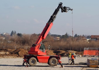 Two workers with a telescopic handler loader assemble concrete slabs for the new building in the...
