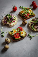 Healthy sandwiches with avocado, tomato, quail eggs, radishes and micro greens (sprouts) on a dark background, hard light