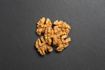 Half of the peeled walnut lies on a textured slate