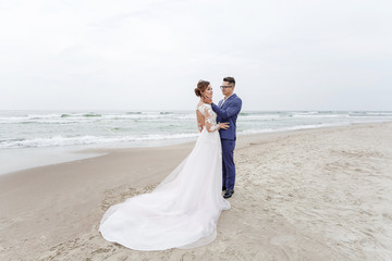 the groom embraces the bride on the sea shore in cloudy weather
