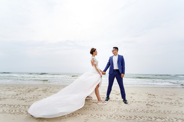 groom holds his bride tightly in a strong wind on the beach