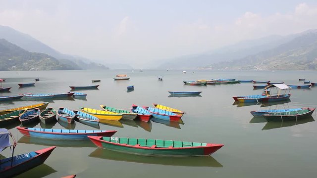 empty multi-colored wooden boats on the lake Phewa on the background of a misty mountain valley
