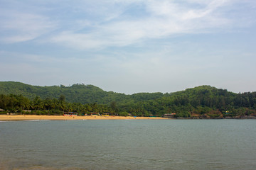 sandy beach with hills, green palm trees and huts, view from the sea