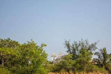 a white catholic church sticks out from behind green trees against a clean blue sky