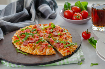 Slices of pizza with greens and salami, cherry tomatoes are on the table.