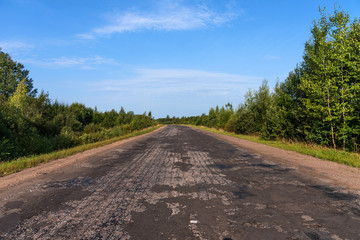 Fototapeta premium Broken empty asphalt country road surrounded by trees in sunny summer day.