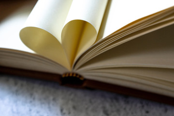 Brown leather vintage notebook blank pages open with pages wrapped in a heart shape form on bright white and gray concrete color texture table top with copy space. Education and studying concept.