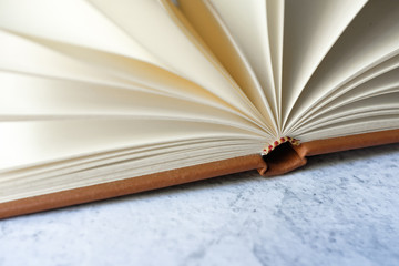 Brown leather vintage notebook blank pages open on bright white and gray concrete color texture table top with empty copy space. Education and studying concept. 
