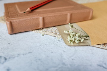 Brown leather vintage notebook, brown craft envelope, dried flower on bright white and gray concrete color texture table top with empty copy space. Education, travelling, letter, romantic concept. 