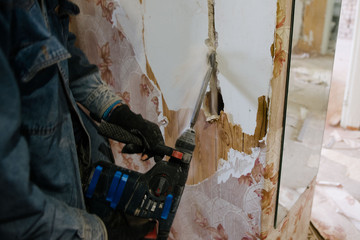 A worker drills a wall using a perforator. Repair in the apartment