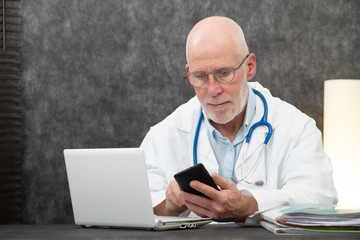 senior bearded doctor reading message on phone