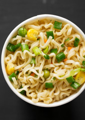 Top view, tasty instant ramen noodles with beef flavoring in a cup over black background. Flat lay, from above, overhead. Close-up.